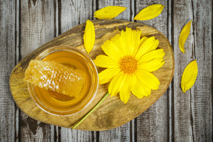 Cutting Board with honey and honeycomb in glass bowl sitting on wooden cutting board with wildflower laying beside it