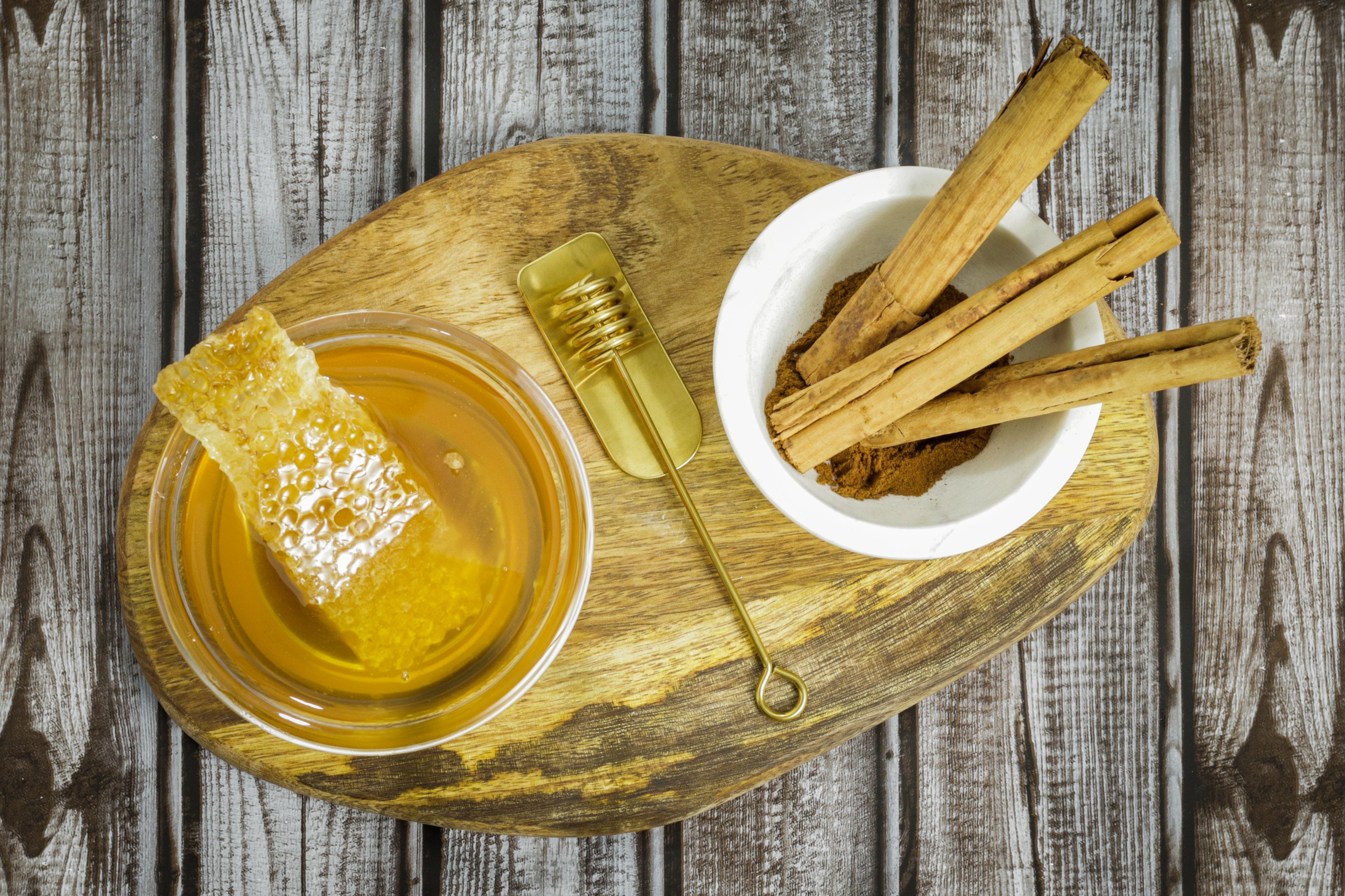Honey In Bowl with Honeycomb Next to Bowl of Ceylon Cinnamon Sticks